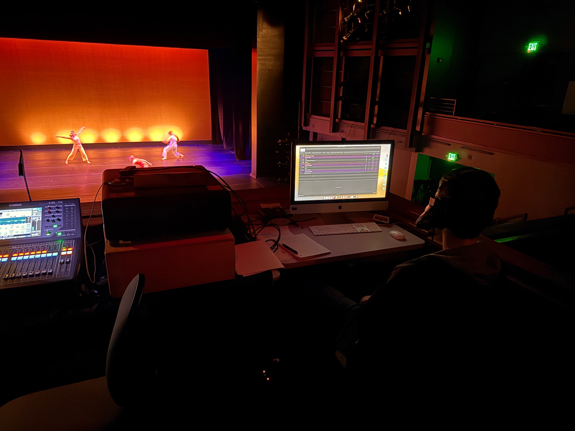 A student mixes a dance performance from front-of-house with a Yamaha console while dancers perform in orange light.