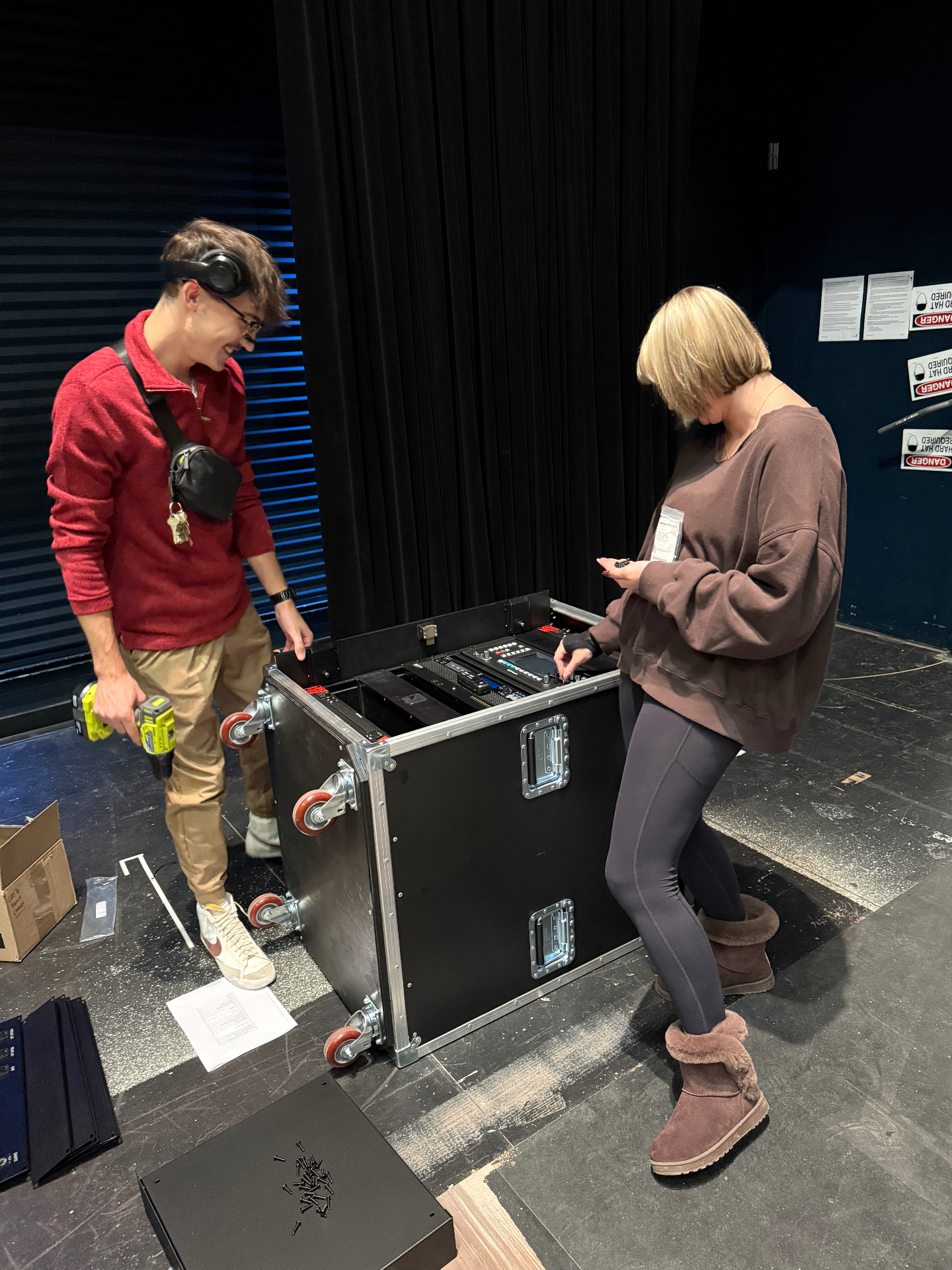 Two Purdue audio technology students assembling a road-case rack of audio gear backstage.