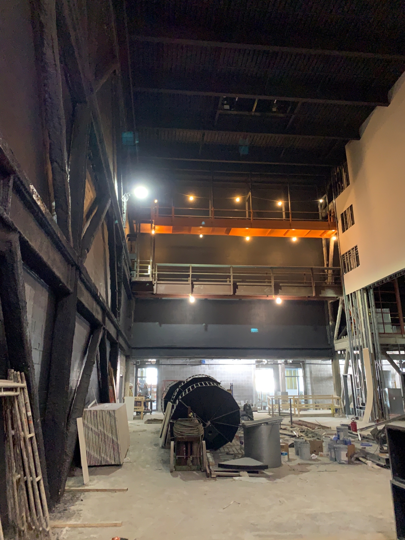 Stage house under construction with steel galleries, a loading bridge, and cable reels staged on the deck below.