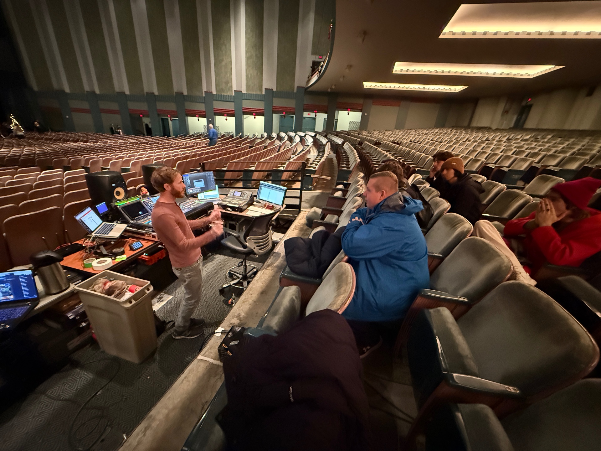 Mercer Aplin at a front-of-house tech table in a large concert hall, working with students at the mix position.
