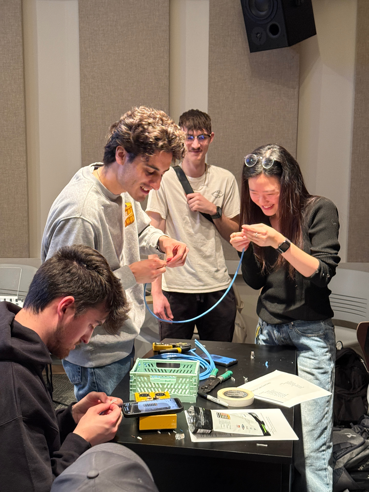 Students terminating Cat6 network cable with crimpers and RJ45 connectors around a lab table in an acoustically treated classroom.