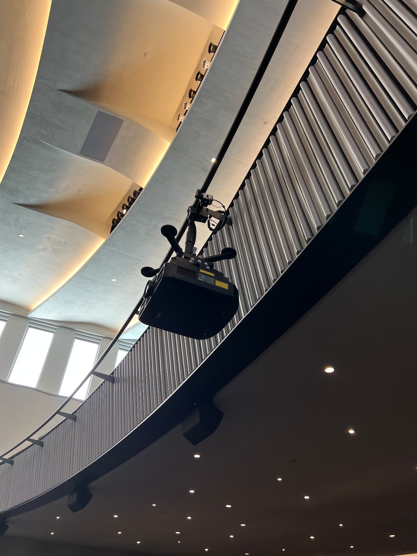 Balcony-rail projector and surround loudspeakers integrated into the ceiling forms.