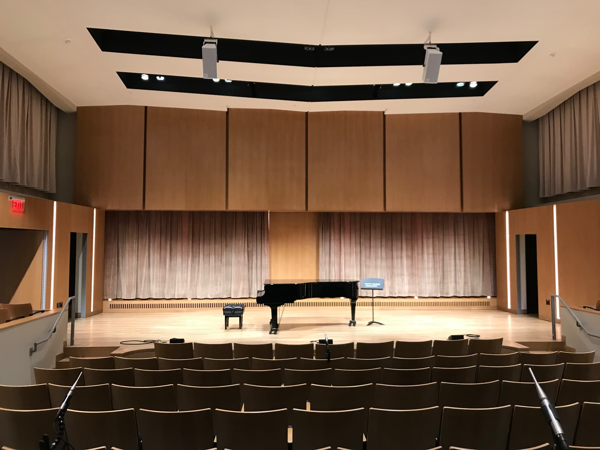 Recital hall with overhead loudspeakers and adjustable acoustic drapery.