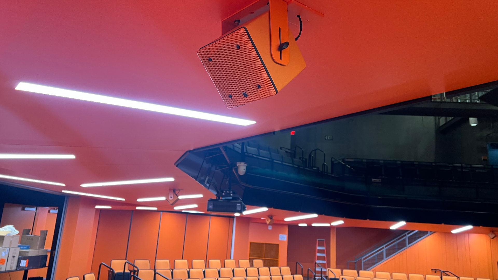 Balcony-soffit fill loudspeaker and projector, color-matched to the architectural finish.