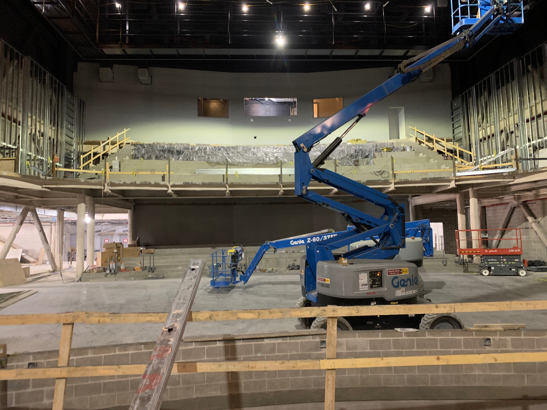 Theater under construction with a boom lift in the orchestra level and the balcony seating tiers still wrapped in protective plastic.