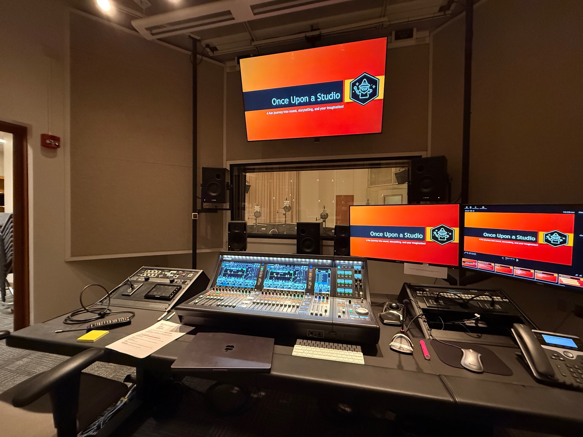 Renovated control room of Purdue's Audio Production Studio with a Yamaha DM7 console, multi-monitor workstation, and 7.1 monitor speakers facing a glass window into the live room.