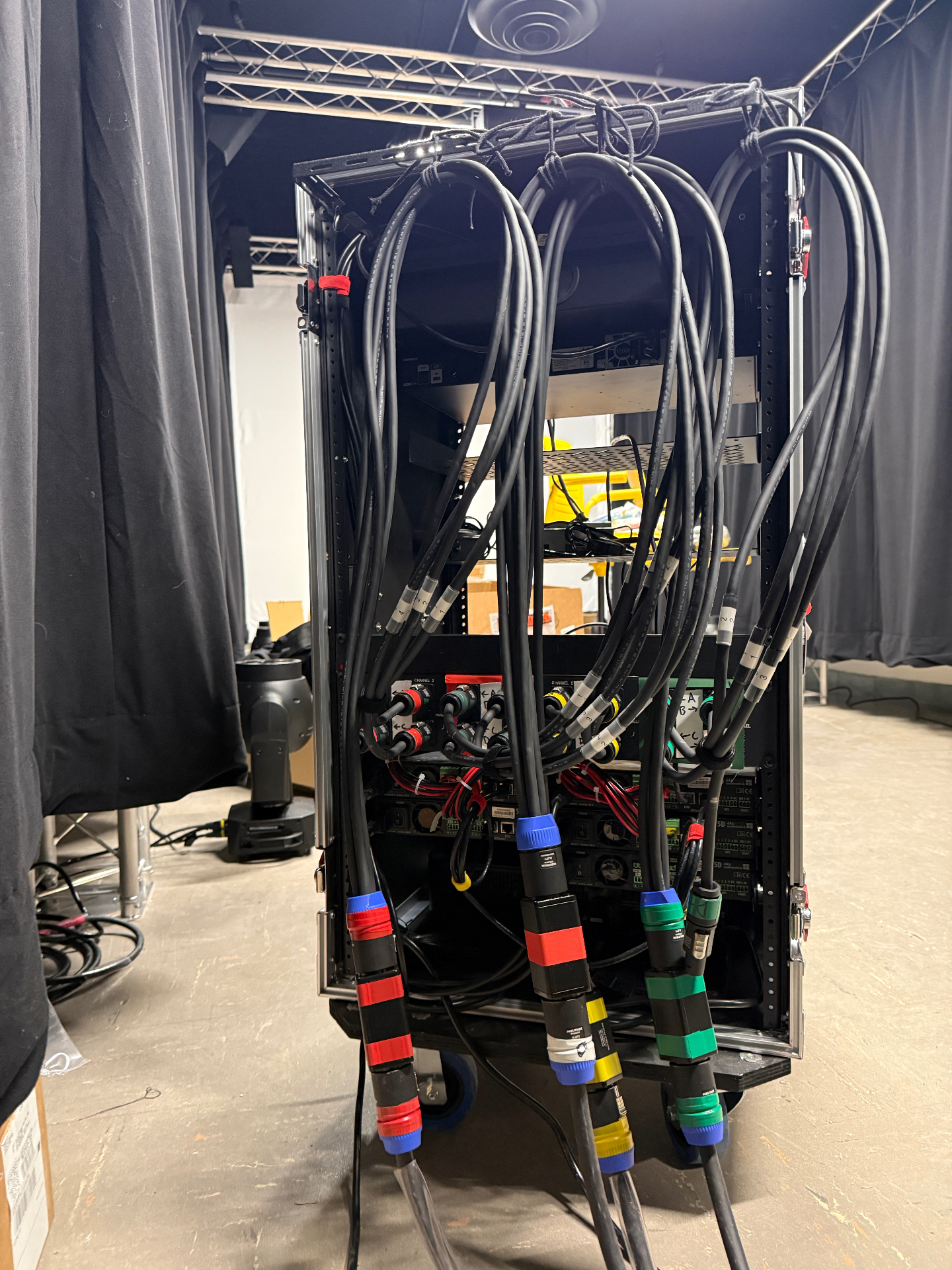 Back of a fully cabled production audio rack with color-coded Powercon and multi-pin connectors during a load-in.